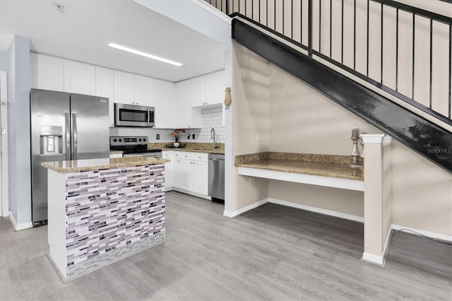 kitchen with light stone counters, stainless steel appliances, light wood-style flooring, white cabinets, and a sink