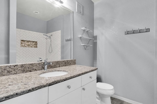 full bath with toilet, vanity, visible vents, baseboards, and tiled shower