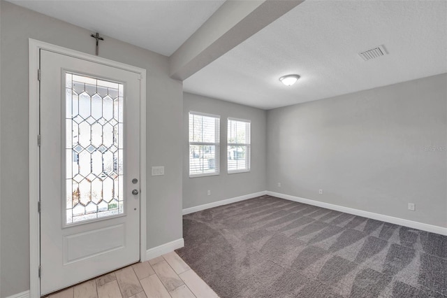 entrance foyer with light colored carpet, visible vents, a textured ceiling, and baseboards