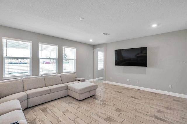 unfurnished living room with light wood-type flooring, baseboards, visible vents, and a textured ceiling