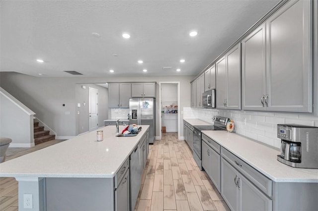 kitchen featuring a center island with sink, stainless steel appliances, recessed lighting, gray cabinets, and light wood-type flooring