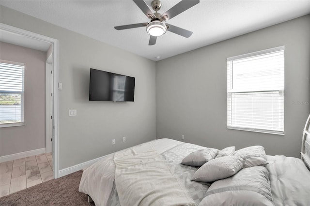 bedroom featuring a textured ceiling, multiple windows, baseboards, and a ceiling fan