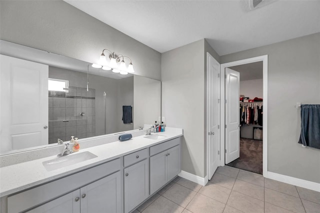 full bath with double vanity, tiled shower, a sink, and a walk in closet