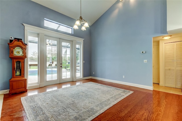 interior space featuring baseboards, a chandelier, wood finished floors, french doors, and high vaulted ceiling