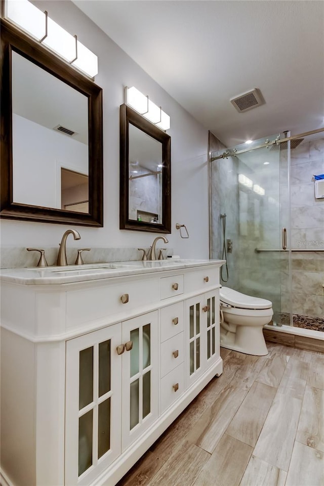 bathroom featuring double vanity, visible vents, toilet, a sink, and a shower stall