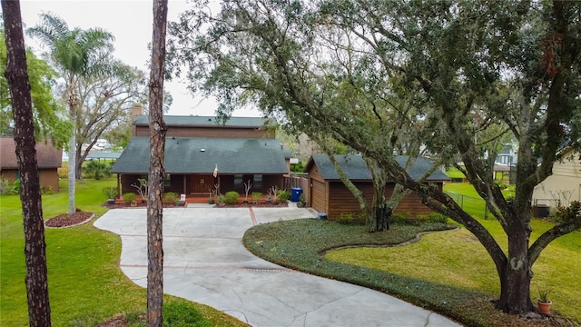 view of front of home featuring roof with shingles, a chimney, a porch, concrete driveway, and a front yard