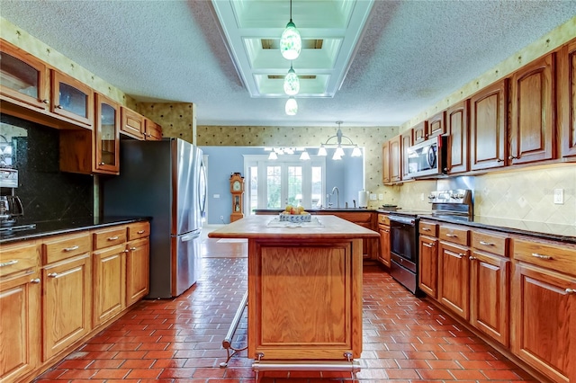 kitchen featuring appliances with stainless steel finishes, glass insert cabinets, a sink, a peninsula, and wallpapered walls