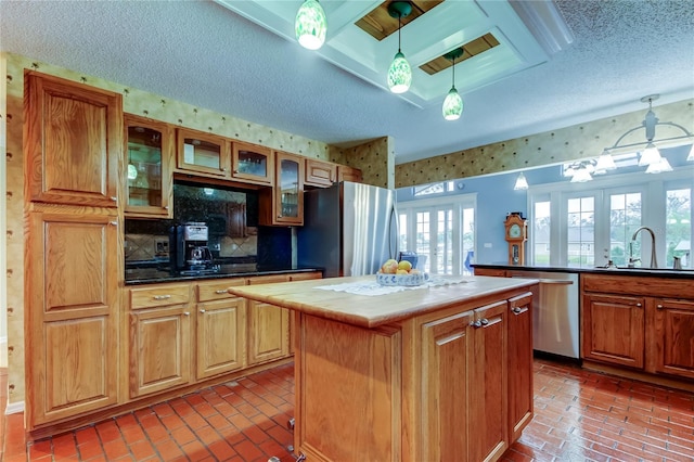 kitchen featuring brick floor, pendant lighting, appliances with stainless steel finishes, a sink, and a kitchen island