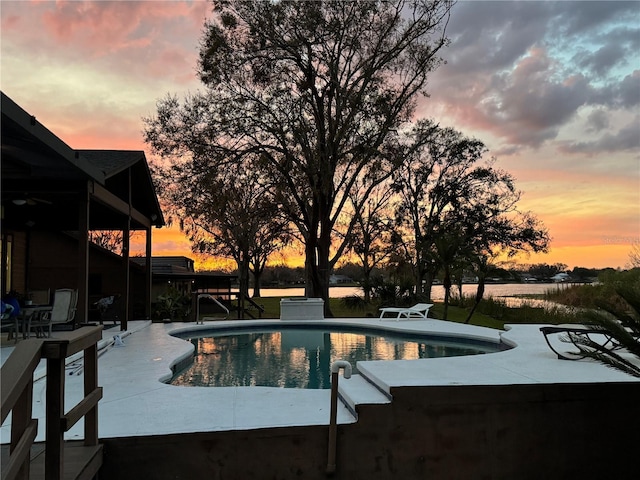 pool at dusk with an outdoor pool and a patio