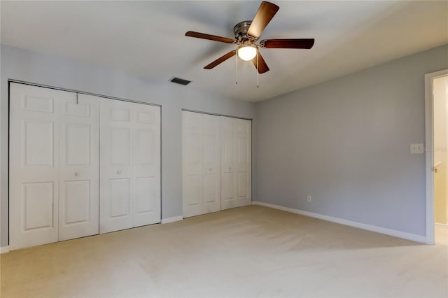 unfurnished bedroom with baseboards, visible vents, light colored carpet, ceiling fan, and two closets