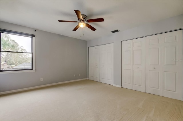 unfurnished bedroom with baseboards, visible vents, light colored carpet, ceiling fan, and multiple closets