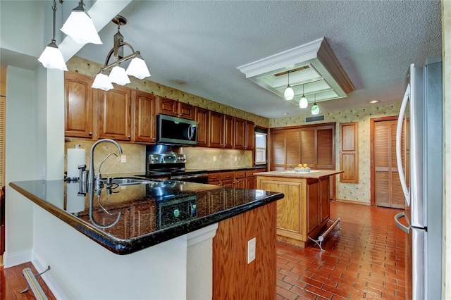 kitchen with brick floor, backsplash, appliances with stainless steel finishes, a sink, and a peninsula