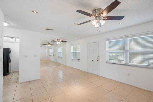 unfurnished room featuring a textured ceiling, a wealth of natural light, and light tile patterned floors