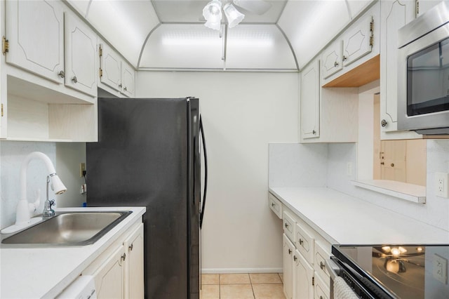 kitchen with light tile patterned floors, sink, black fridge, and white cabinets