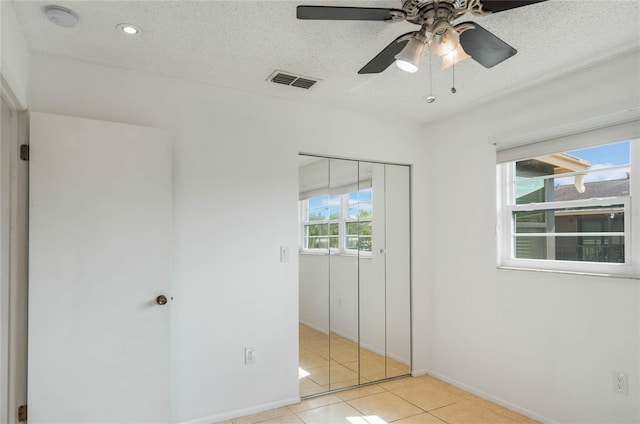 unfurnished bedroom with ceiling fan, light tile patterned floors, a textured ceiling, and a closet