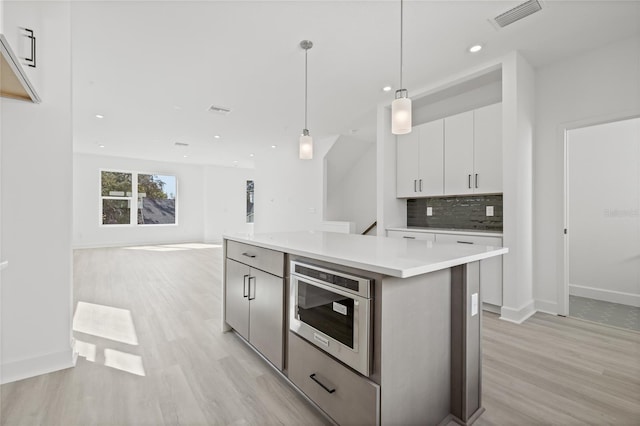 307 15th St N, Saint Petersburg, FL 33705 - kitchen featuring visible vents, built in microwave, light wood-type flooring, white cabinetry, and backsplash