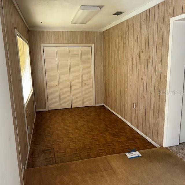 unfurnished bedroom featuring wood walls, dark parquet flooring, and a closet