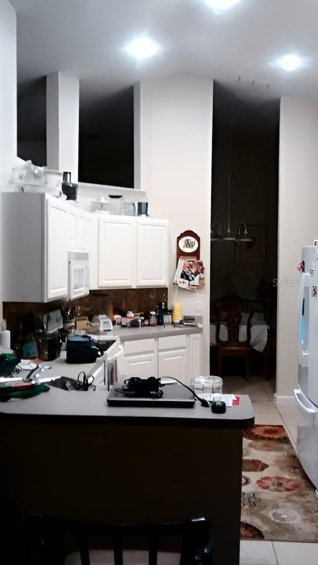 kitchen with a peninsula, white appliances, light tile patterned floors, and white cabinets