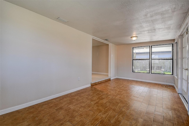 spare room featuring a textured ceiling, wood finished floors, visible vents, and baseboards