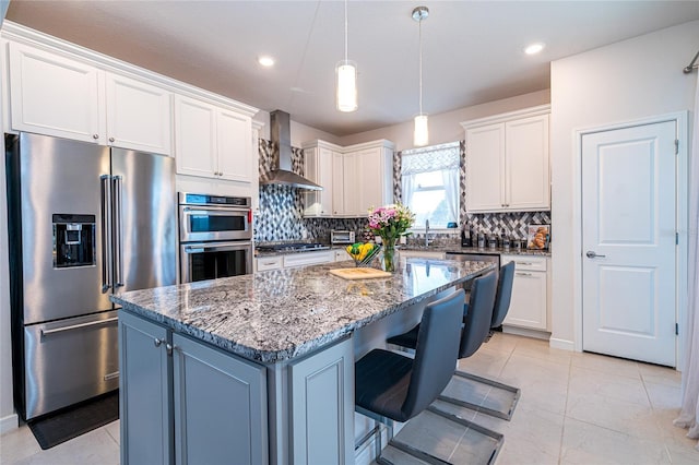 kitchen with stainless steel appliances, wall chimney exhaust hood, white cabinetry, and a center island