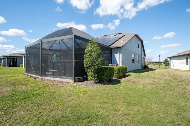 back of house with a lanai, stucco siding, solar panels, and a yard