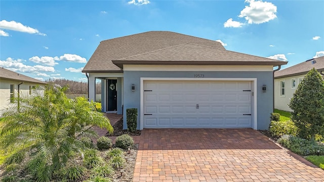 view of front facade featuring an attached garage, roof with shingles, decorative driveway, and stucco siding