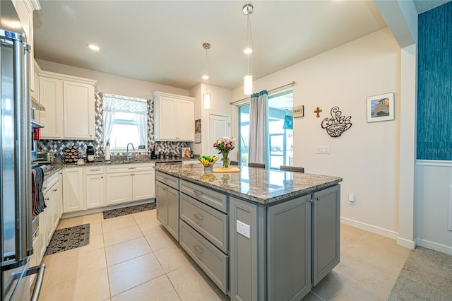 kitchen featuring tasteful backsplash, a center island, light stone countertops, gray cabinetry, and white cabinetry