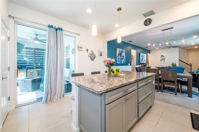 kitchen with light stone counters, gray cabinetry, visible vents, hanging light fixtures, and a center island