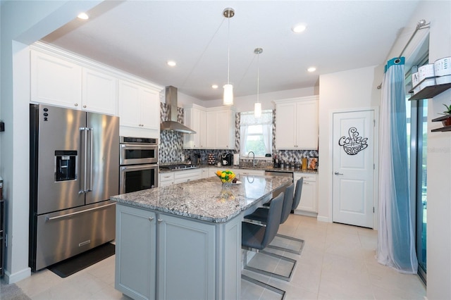 kitchen with a breakfast bar, white cabinetry, appliances with stainless steel finishes, a center island, and wall chimney exhaust hood