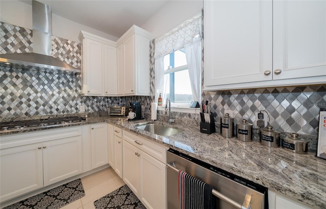 kitchen featuring light stone counters, a sink, white cabinets, appliances with stainless steel finishes, and wall chimney exhaust hood