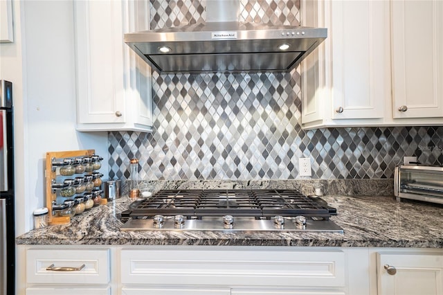 kitchen with tasteful backsplash, stainless steel gas stovetop, white cabinetry, dark stone counters, and wall chimney exhaust hood