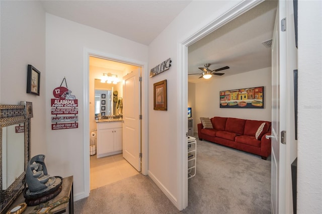 hall featuring light carpet, baseboards, and visible vents