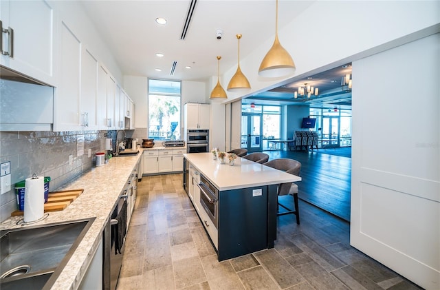 kitchen with decorative light fixtures, light countertops, backsplash, white cabinetry, and a kitchen breakfast bar