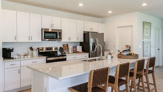 kitchen featuring white cabinetry, a center island with sink, stainless steel appliances, and a breakfast bar