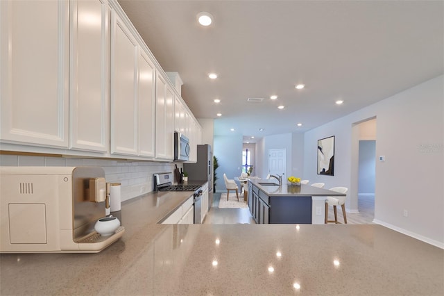 kitchen with an island with sink, white cabinetry, stainless steel appliances, and decorative backsplash