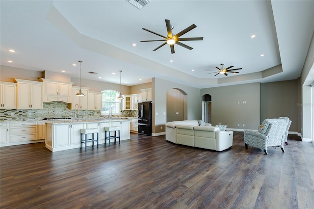 living room with a tray ceiling, ceiling fan, sink, and dark hardwood / wood-style floors