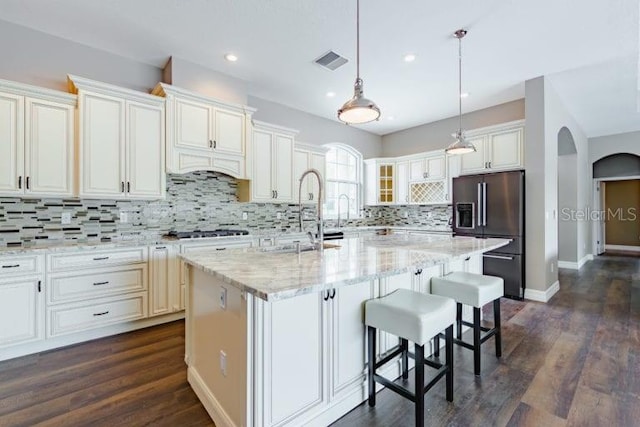 kitchen with appliances with stainless steel finishes, hanging light fixtures, light stone countertops, a breakfast bar area, and a kitchen island with sink