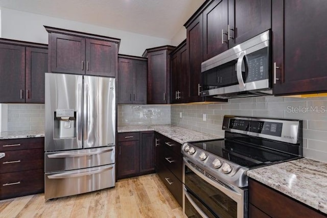 kitchen with appliances with stainless steel finishes, light hardwood / wood-style flooring, light stone counters, dark brown cabinetry, and backsplash