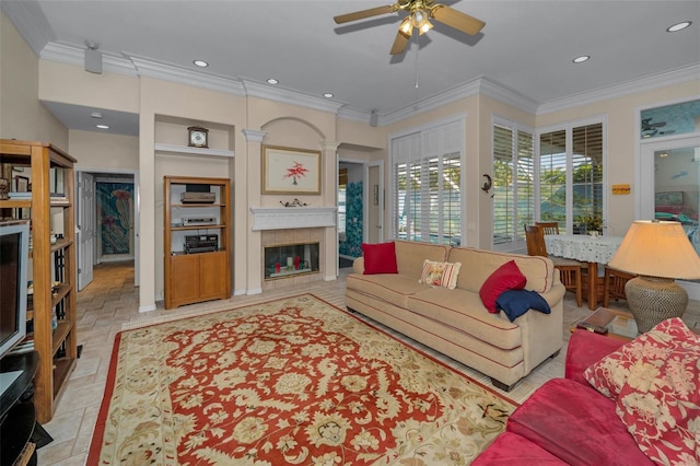 living room with built in shelves, ornamental molding, a ceiling fan, a glass covered fireplace, and recessed lighting