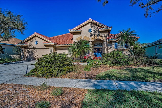 mediterranean / spanish home with a tile roof, an attached garage, driveway, and stucco siding