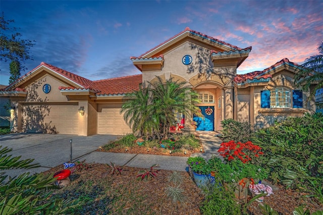 mediterranean / spanish home featuring a tile roof, stucco siding, an attached garage, and concrete driveway