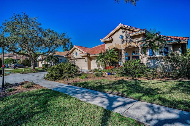 mediterranean / spanish-style home featuring a tile roof, stucco siding, a front yard, and a garage