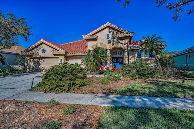 mediterranean / spanish home featuring stucco siding, a tile roof, a garage, and concrete driveway