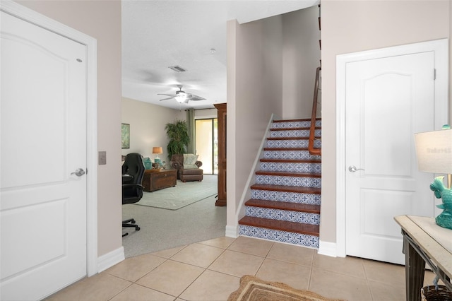 stairway featuring tile patterned flooring, visible vents, a ceiling fan, baseboards, and carpet