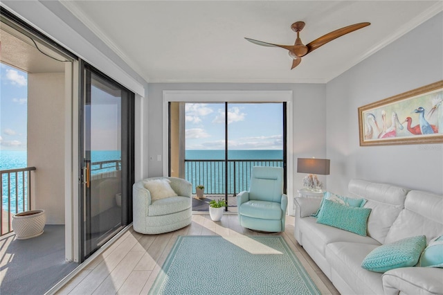 living room featuring light wood finished floors, ornamental molding, a water view, and a ceiling fan