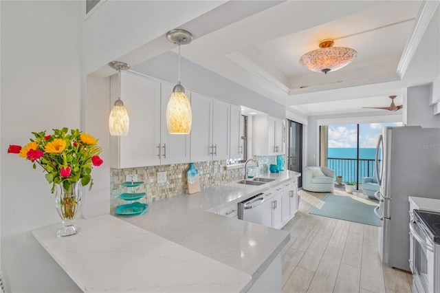 kitchen with appliances with stainless steel finishes, backsplash, light stone countertops, a tray ceiling, and a sink