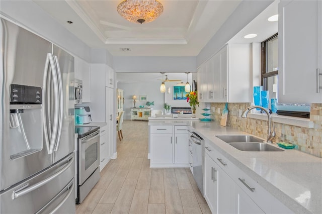 kitchen with a sink, white cabinets, appliances with stainless steel finishes, tasteful backsplash, and a raised ceiling