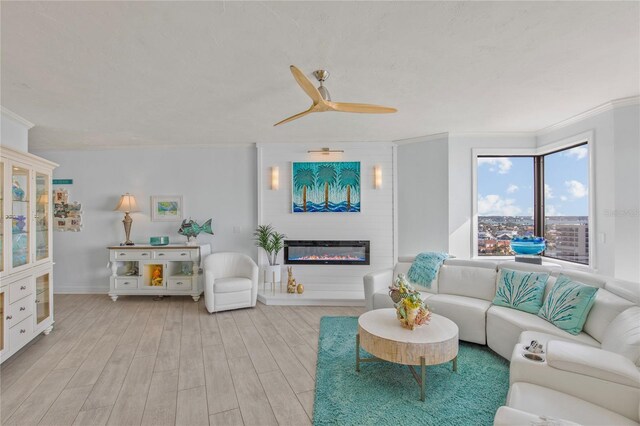 living area featuring ornamental molding, a large fireplace, ceiling fan, wood finished floors, and baseboards