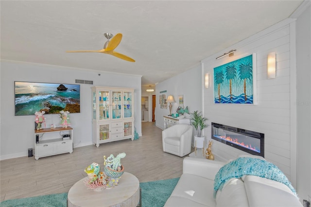 living area with wood finished floors, a glass covered fireplace, visible vents, and baseboards