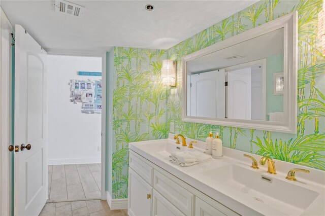 bathroom with double vanity, visible vents, a sink, baseboards, and wallpapered walls